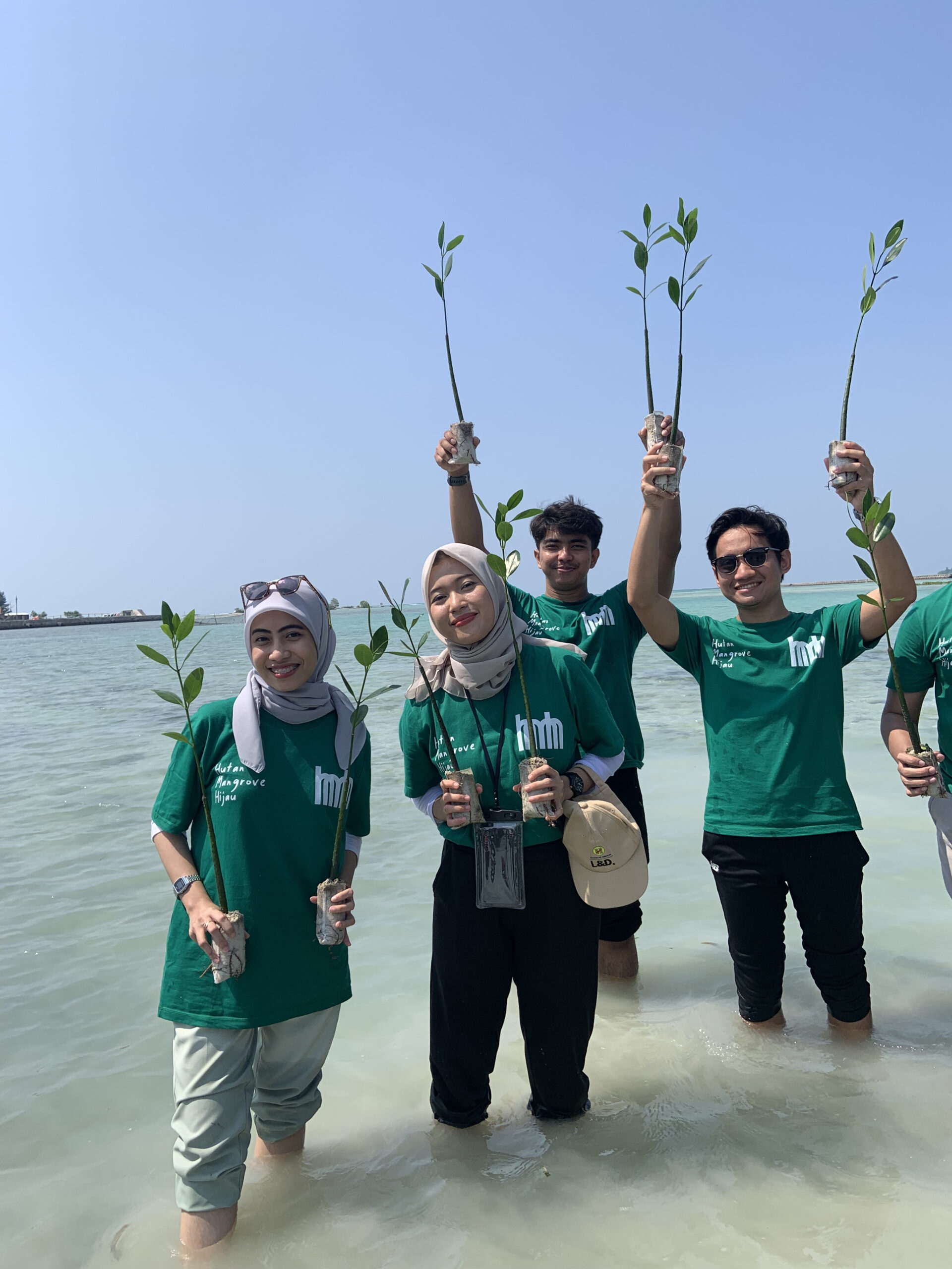 2 wanita dan 2 pria peserta gathering kantor dengan seragam kaos hijau Bumi Journey memegang benih-benih bakau pada kedua tangan mereka